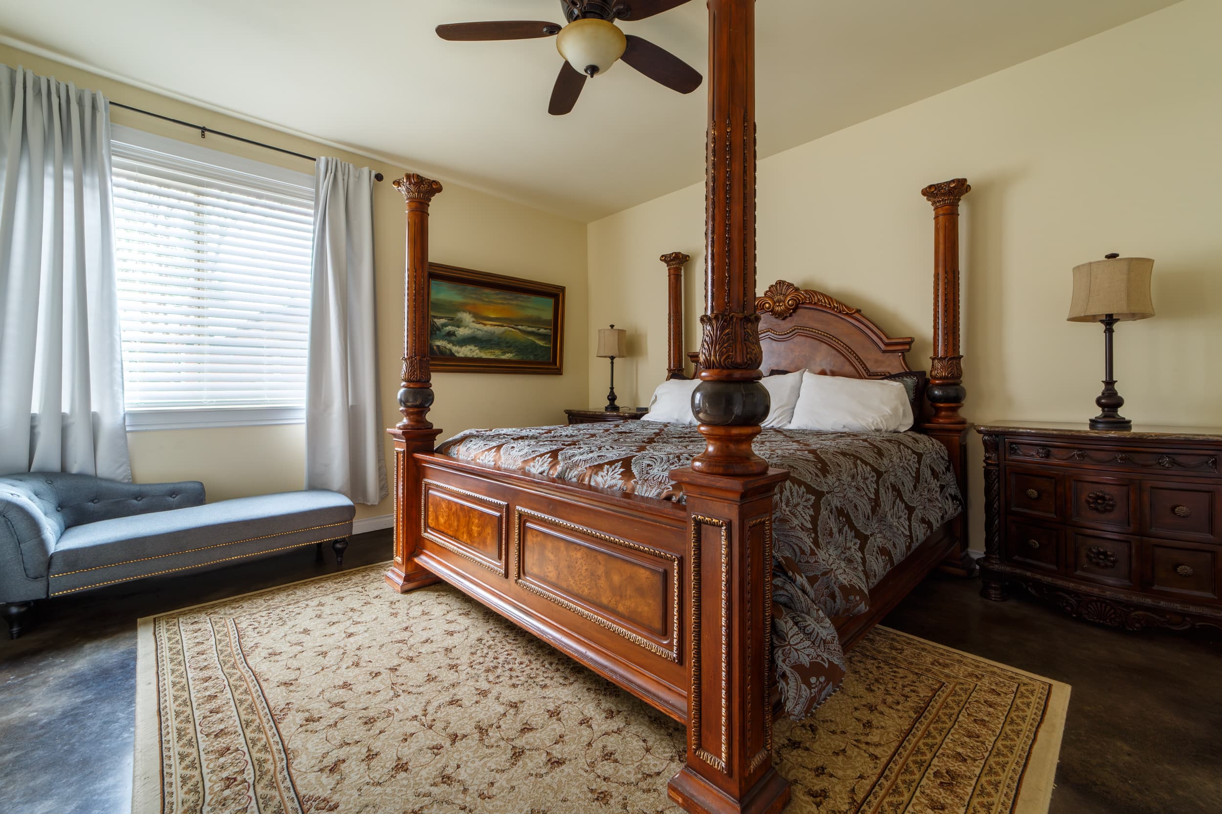 A detailed wood-carved king bed with a high arched headboard and a copper patterned bedspread, flanked by dark wood nightstands and lamps.