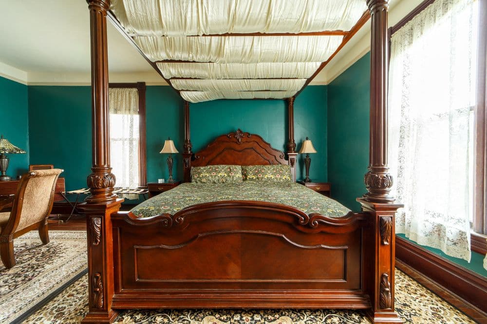 A classic bedroom featuring a wooden four-poster bed, a patterned bedding set, and teal walls.