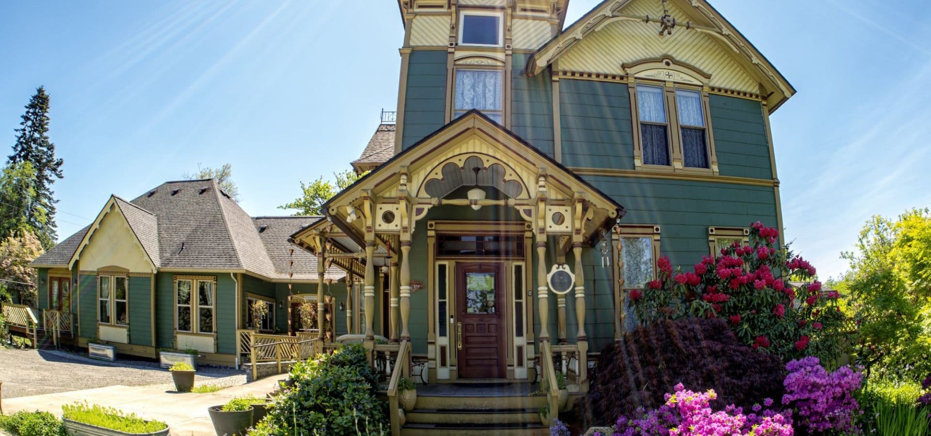 Victorian-style green house with ornate details and colorful flowers in the foreground.